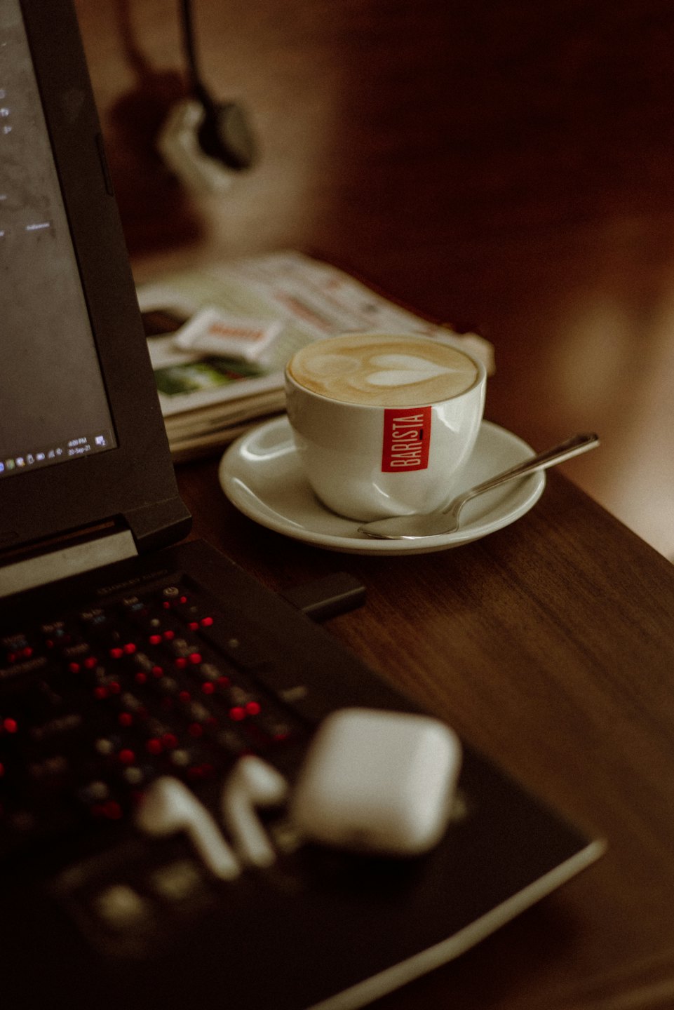 Laptop, latte art, and earbuds on a wooden table.